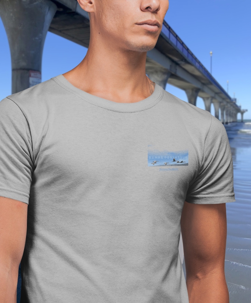 Front view of the chest badge print on a grey Surface Active spotted shags, Banks Peninsula, Canterbury, New Zealand t-shirt worn by a man photographed alongside New Brighton pier. 
